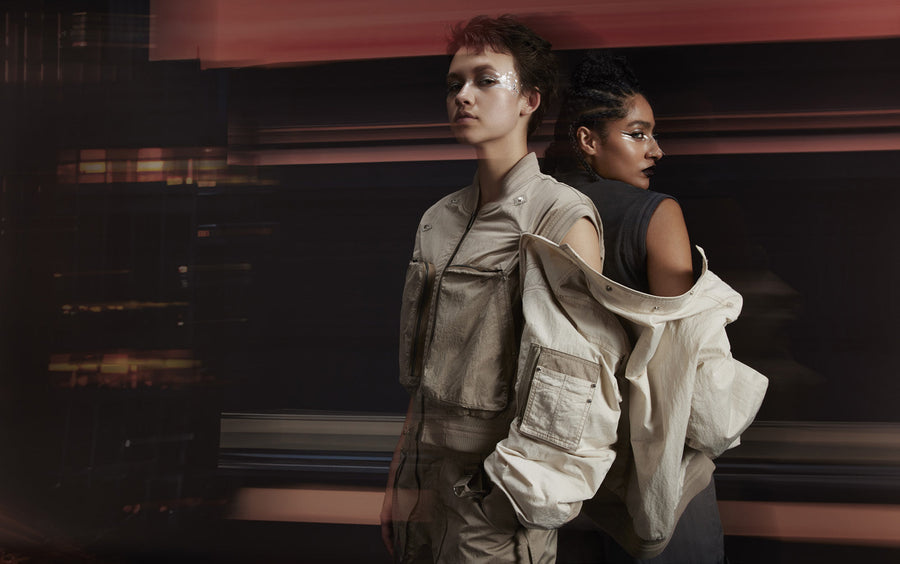 Two figures back to back in beige FENGGY outerwear, one jacket easing off the shoulder to show its modular construction.