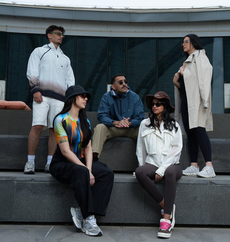 Five figures in NeoSpherium District outerwear on granite steps outside a curved glass building, in overcast daylight.