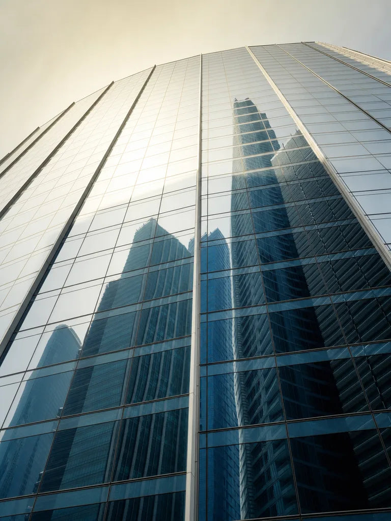 A glass tower with the city's other towers reflected in its facade, the loudest names, mirrored back, before anything new becomes visible.