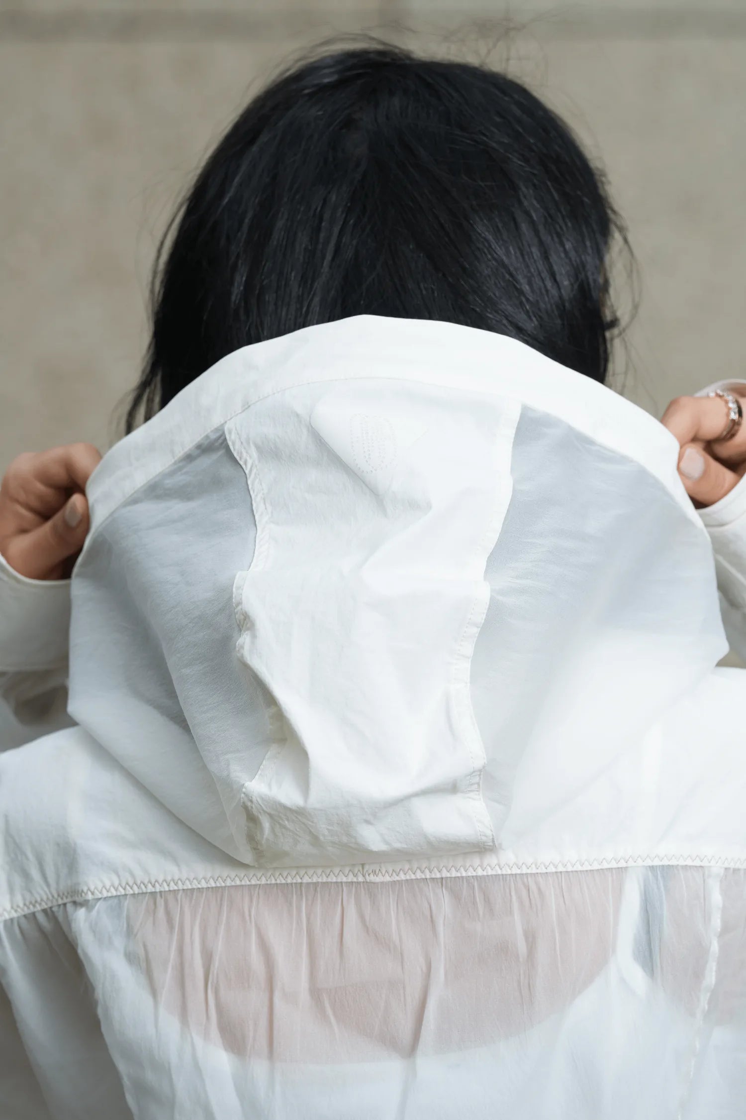 A woman in a white FENGGY nylon hooded windbreaker, hood drawn up, back to camera, the garment moving with her.