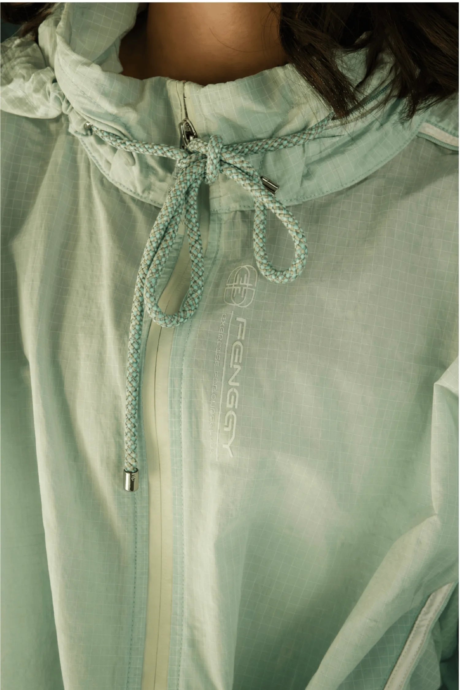 A macro of a FENGGY mint ripstop windbreaker, braided drawcord at the neckline, embossed FENGGY logo, the line the cutting was patient about.
