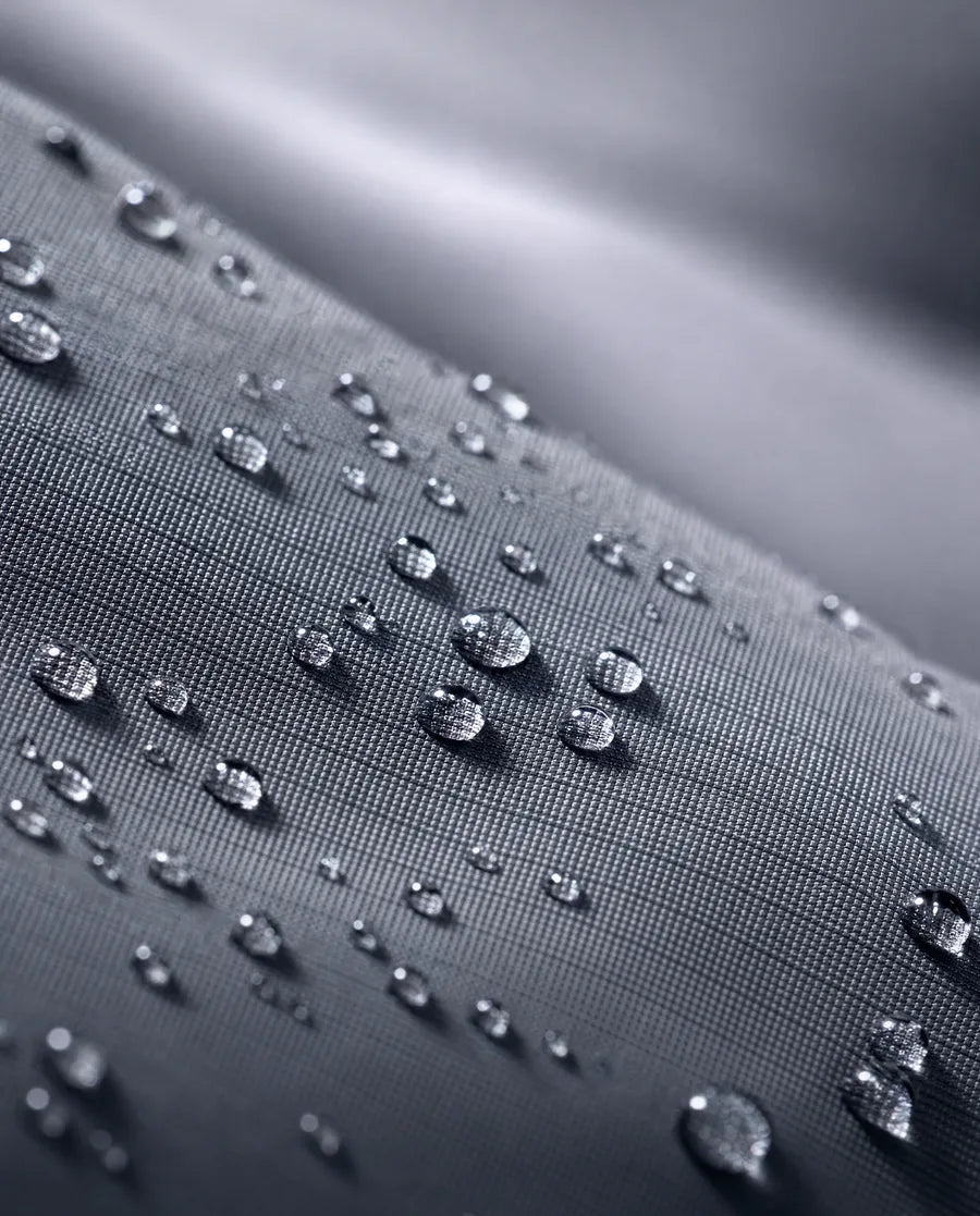 Macro of water droplets beading on a tightly woven slate-gray nylon ripstop