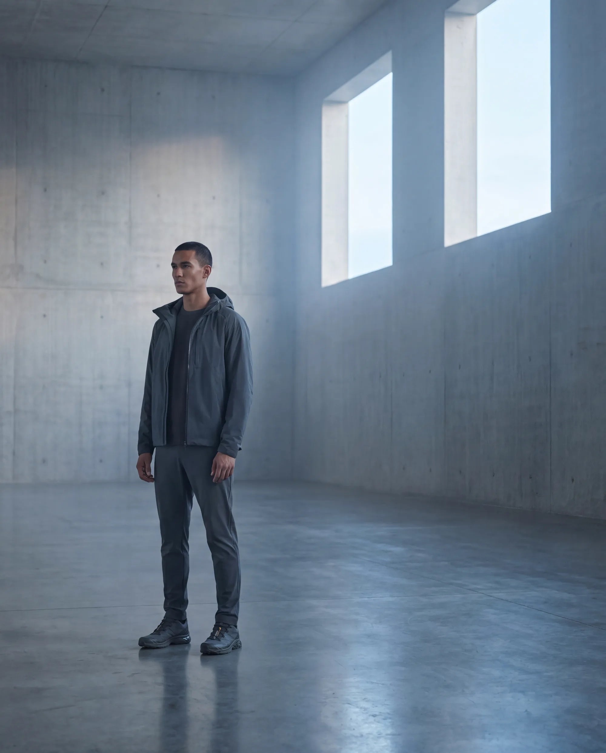 A composed figure standing still in a soft gray field of light.